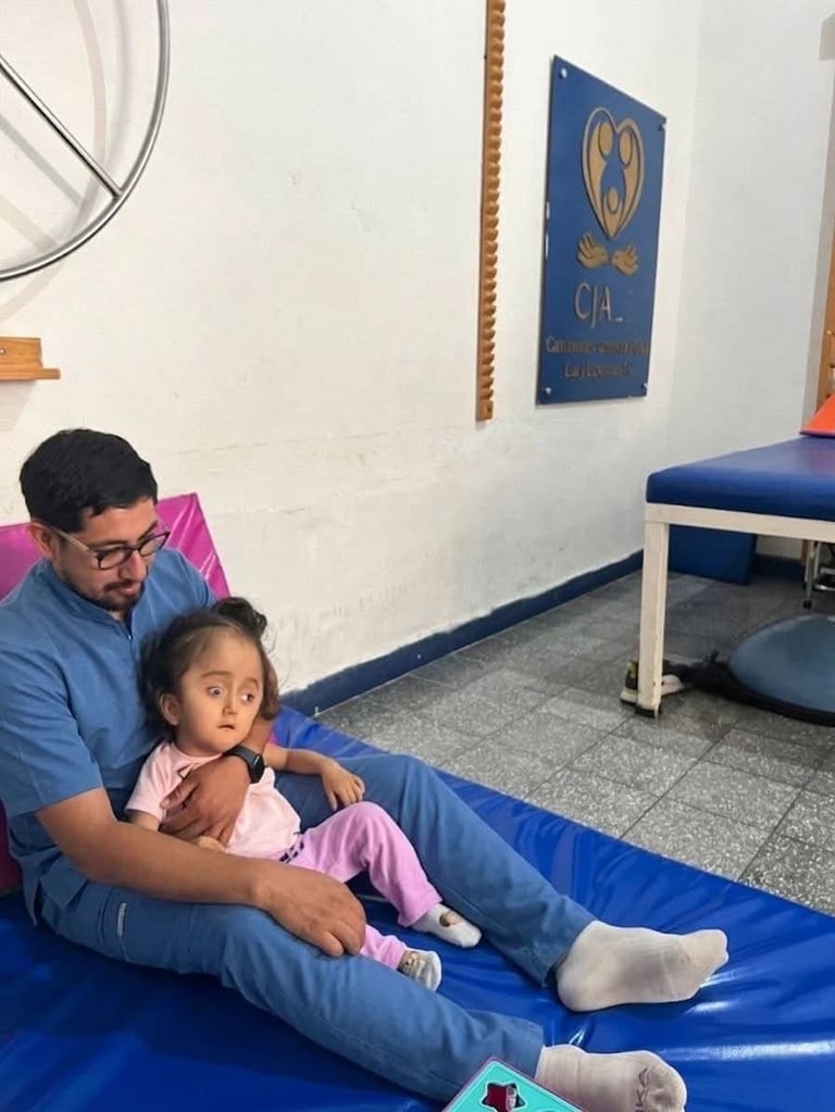 Adult man and young child sitting together on blue exercise mat in gym with equipment visible in background