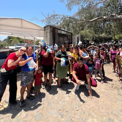 Large outdoor gathering of people in a courtyard, many wearing colorful clothing, with tents and trees visible