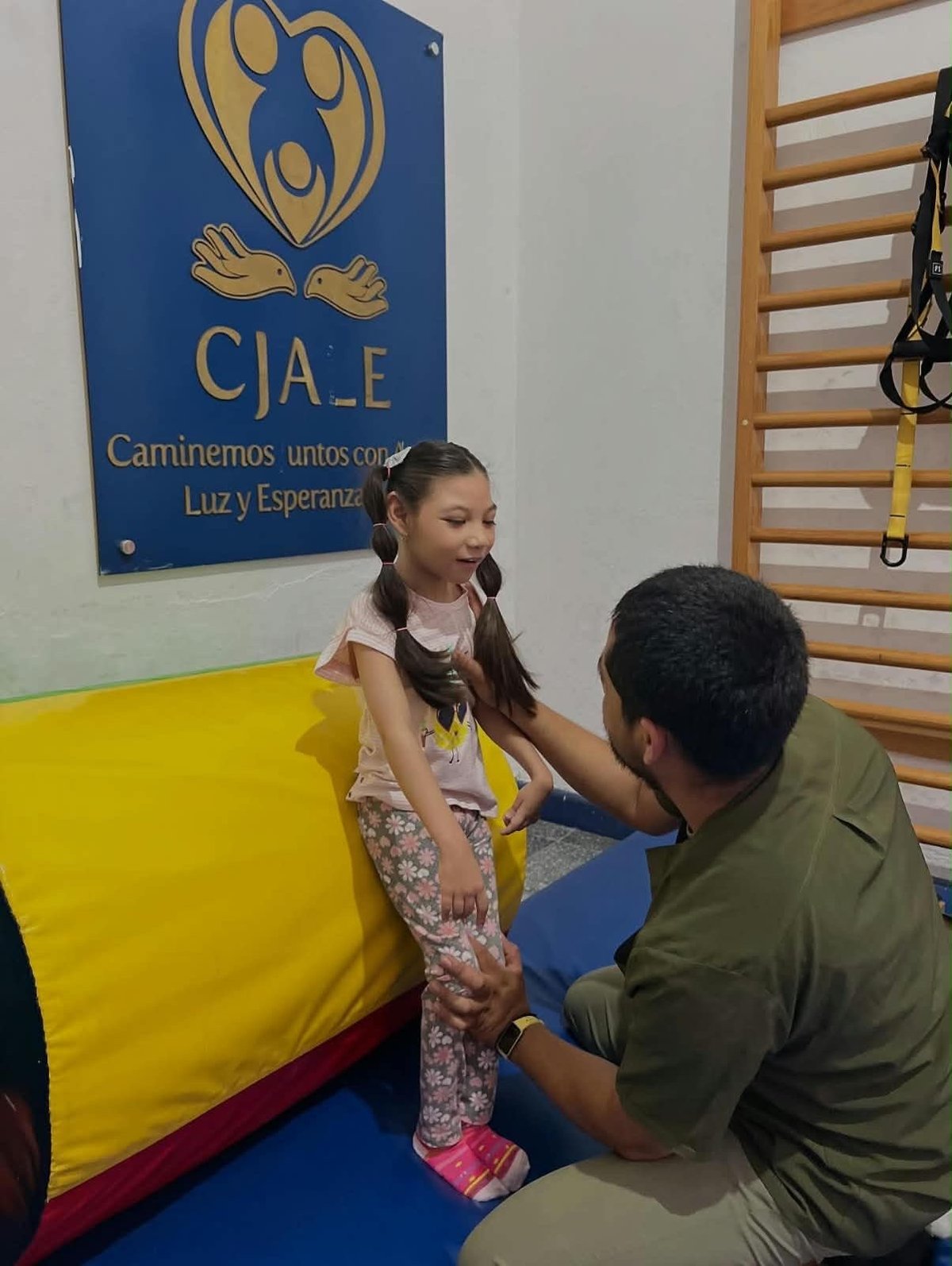Adult male instructing young girl on gymnastics mat in gym with blue CJAE logo sign on wall