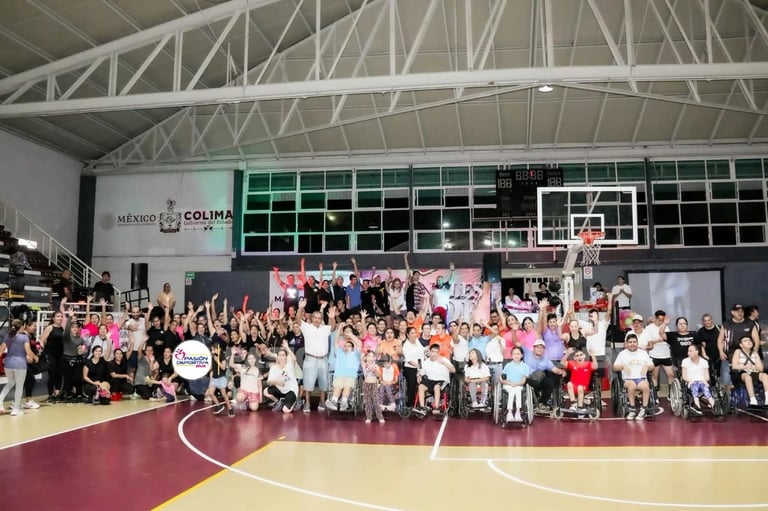 Large group of people gathered on a basketball court in an indoor gymnasium with a stage and decorated backdrop